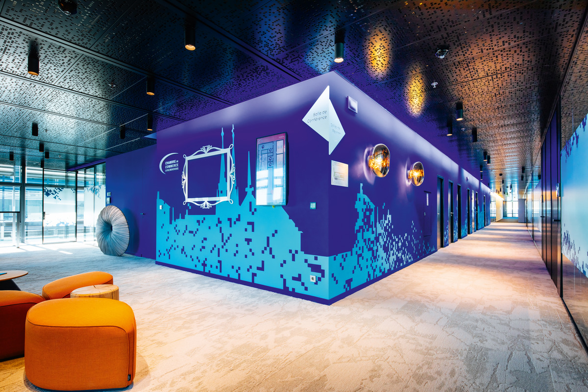 Luxembourg’s skyline is applied as a visual repeatedly referenced below the matte black ceiling with its perforated steel lagging as colorful grids in the carpets or pixel-like, sporadic silhouettes on walls painted a vibrant blue.